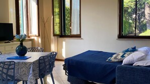 A room with a bed, a table with chairs, a radiator, and a window with curtains. - Verona Blue Suite: Comfort & Parking Space Between Arena & Fairgrounds (Verona)