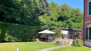 A well-maintained garden with a patio area, a covered seating area, and a building with a red facade. - Verona Blue Suite: Comfort & Parking Space Between Arena & Fairgrounds (Verona)
