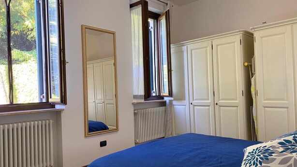 A bedroom with a large bed, two windows with curtains, a radiator, and white wardrobes. - Verona Blue Suite: Comfort & Parking Space Between Arena & Fairgrounds (Verona)