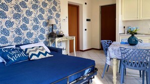 A bedroom with a blue bed, a bedside table with a lamp, and a wall with a tropical leaf pattern. - Verona Blue Suite: Comfort & Parking Space Between Arena & Fairgrounds (Verona)