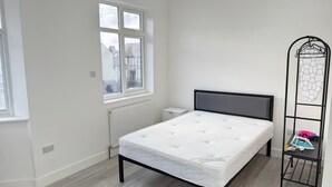 Quarto com cama, radiador, janela e tábua de passar roupa de metal.