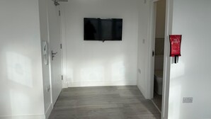 Um corredor com televisão de tela plana na parede, manta anti-fogo também na parede e uma porta à direita.