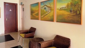 Aulassa on vastaanottotiski, kolme rottinkituolia, joissa on keltaiset tyynyt, sekä kolme maisemamaalausta seinällä.