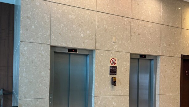 Moderni hissiaula, jossa on kaksi hissiä, digitaalinen näyttö, jossa näkyy numero 4, ja tupakointikieltokyltti.
