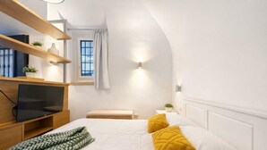 Ein modernes Schlafzimmer mit einem Bett, einem Fernseher, einem Regal mit Dekoration und einem Fenster mit Vorhängen.