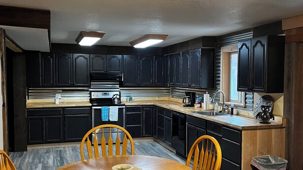 A modern kitchen with dark cabinetry, a central island, and a dining area with wooden chairs and a table. - Tobacco Riverwalk Condo - Eureka, MT (Eureka)