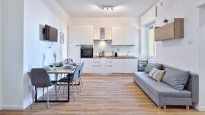 Une cuisine moderne avec des meubles blancs, un coin repas comprenant une table et des chaises, et un canapé gris.