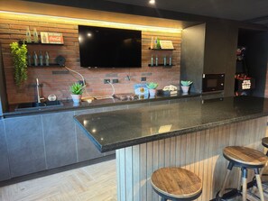 A modern kitchen with a flat-screen TV, a brick backsplash, and a bar area with stools.