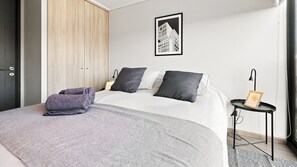 A modern bedroom with a bed, pillows, a bedside table, a lamp, and a framed picture on the wall. - Oceana Suites Toesca (Santiago)