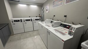 A laundry facility with multiple washing machines and dryers, a control panel, and safety signs on the wall. - Oceana Suites Toesca (Santiago)