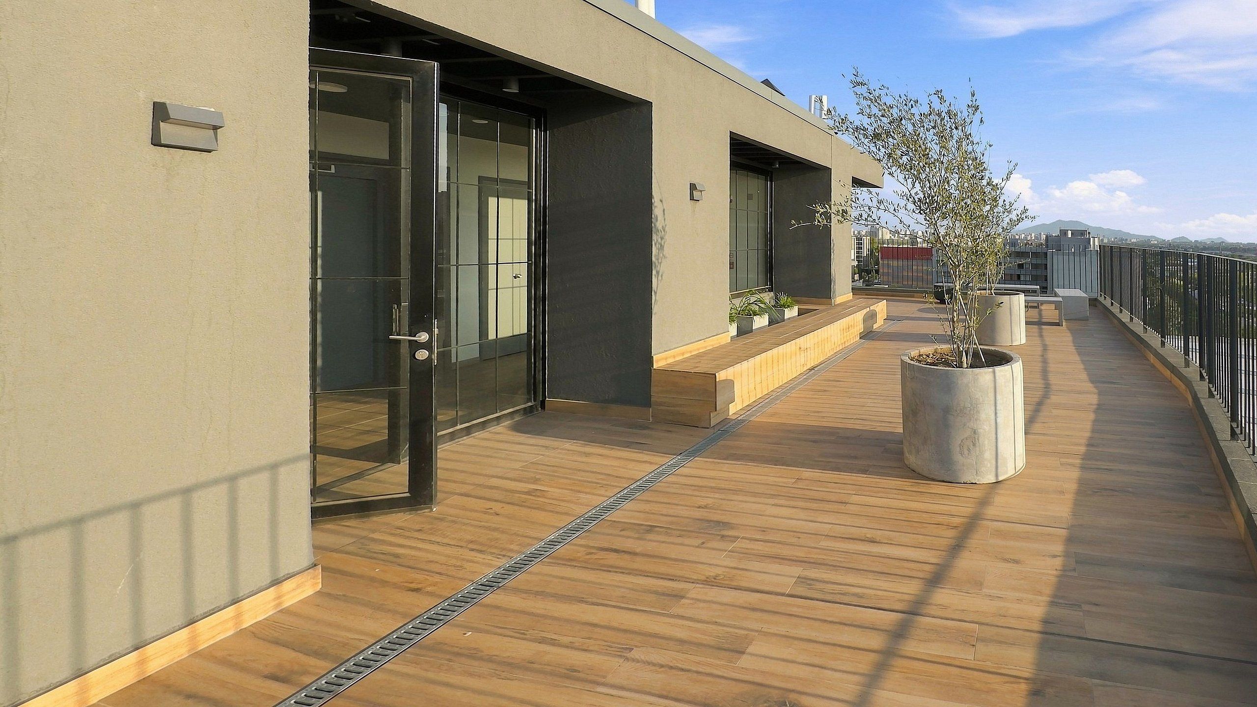 A modern building with a wooden deck, glass doors, and potted plants.