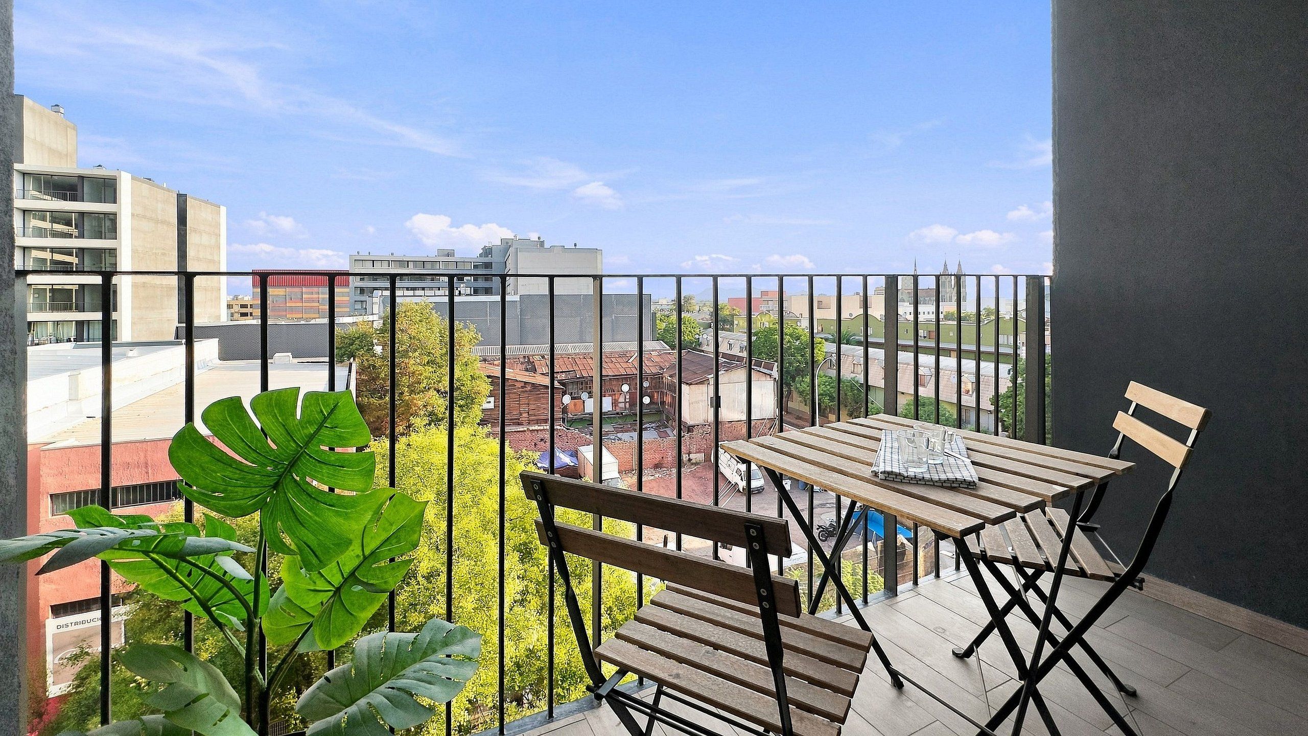 A balcony with a table and chairs, a view of the cityscape, and a large plant.