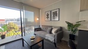 A modern living room with a sofa, a coffee table, and a balcony with outdoor furniture. - Oceana Suites Toesca (Santiago)