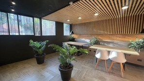 A modern interior with a wooden ceiling, large windows, a seating area, and potted plants.