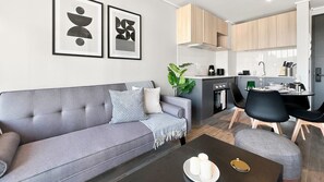 A modern living room with a grey sofa, a coffee table, and a dining area with a chair and table. - Oceana Suites Toesca (Santiago)
