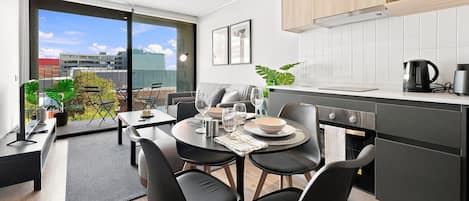 A modern kitchen with a dining area, a view of the city, and a balcony with plants.