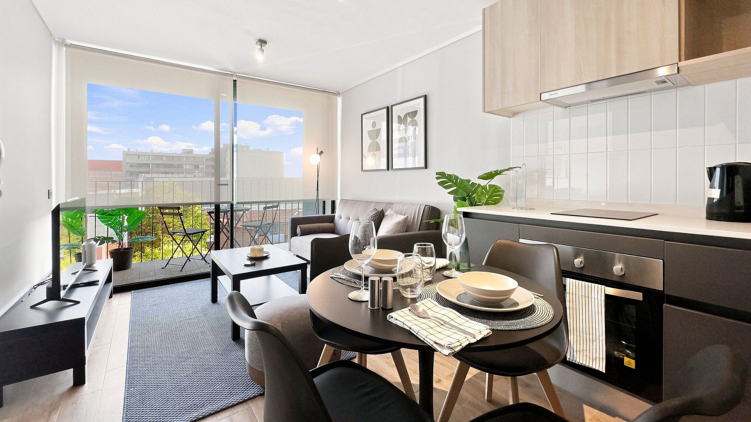 A modern kitchen with a dining area, a balcony with plants, and a view of the city.
