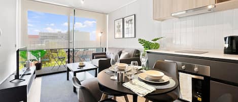 A modern kitchen with a dining area, a balcony with plants, and a view of the city.