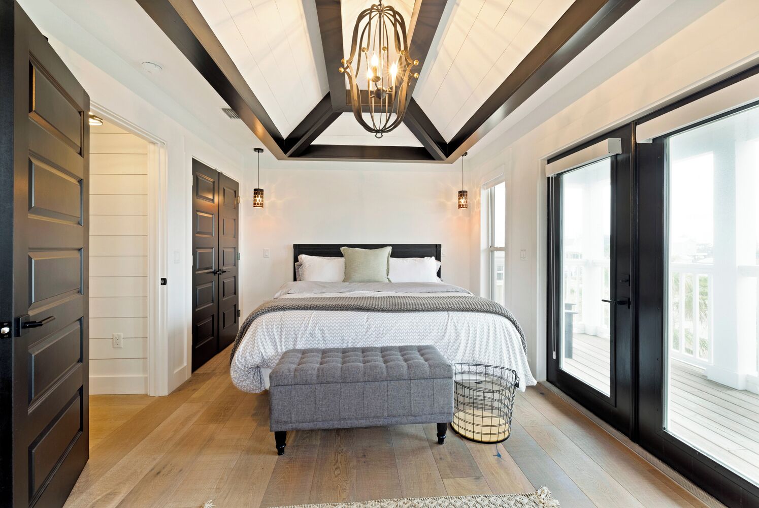 Een slaapkamer met een groot bed, een bankje, een kroonluchter en uitzicht door een schuifdeur.