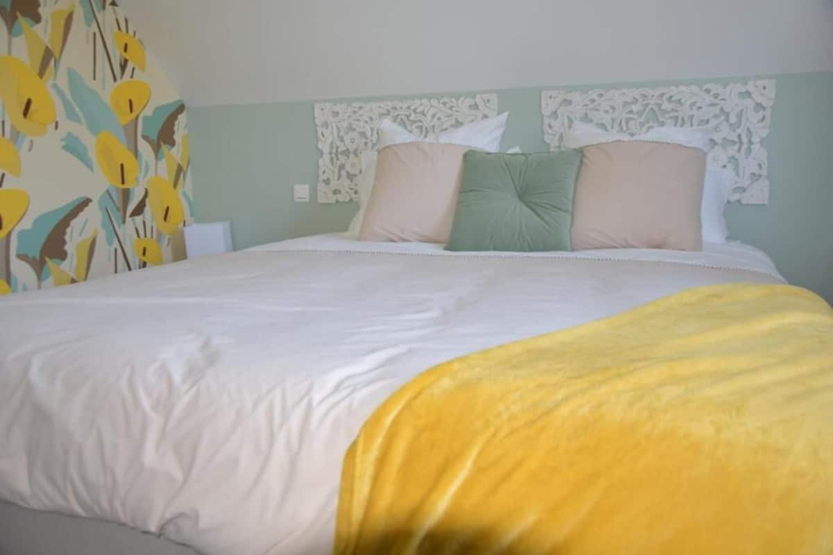 Un lit avec une couverture blanche et jaune, un oreiller vert et un oreiller beige.