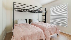 Quarto com beliche, duas camas de solteiro, janela com persianas e piso de madeira.