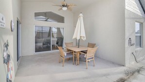 Um alpendre coberto com mesa e cadeiras, um ventilador de teto e uma janela grande.