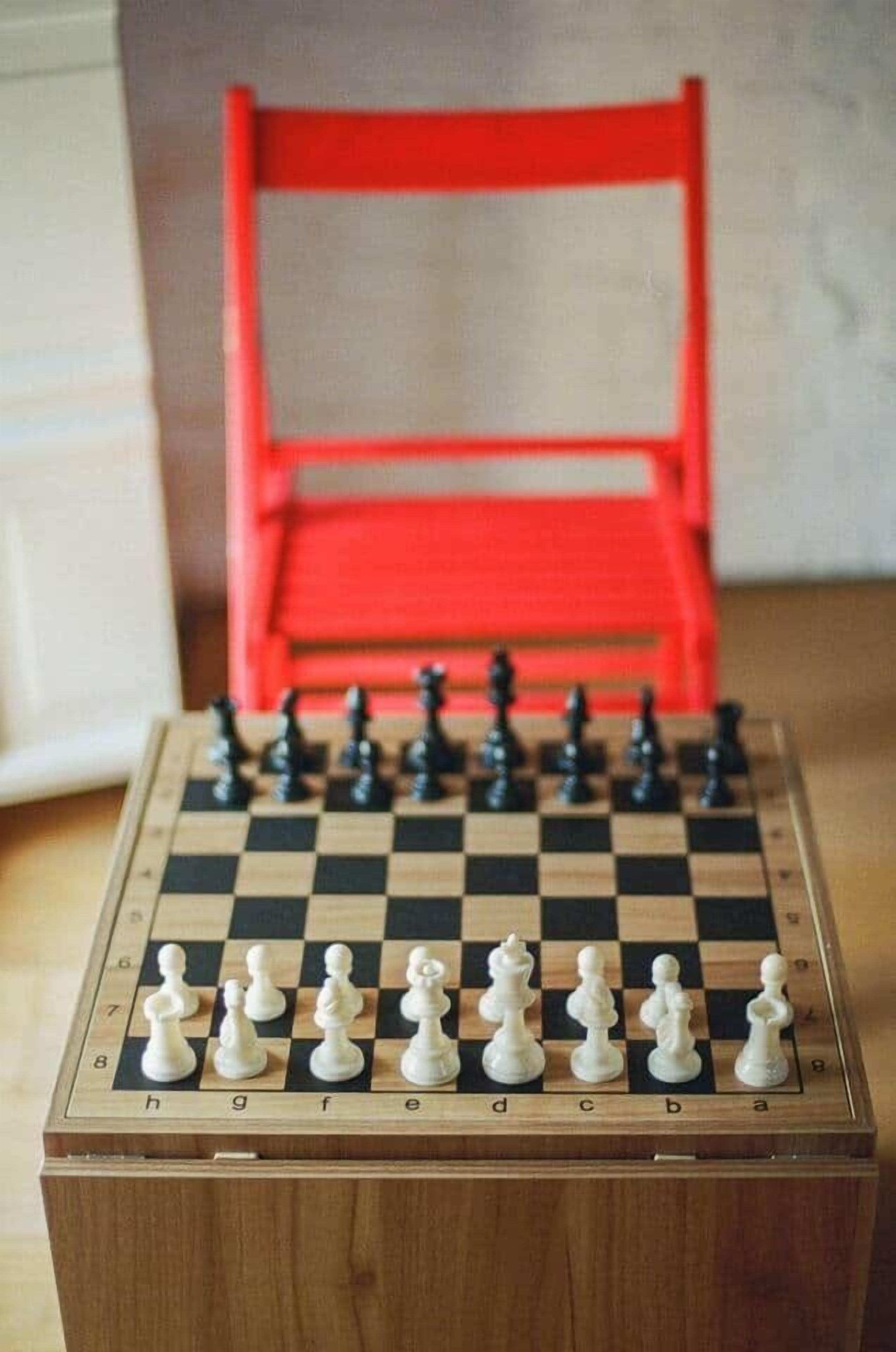 Een schaakbord met opstelling voor een spel, geplaatst op een houten tafel in een kamer met een rode stoel op de achtergrond.