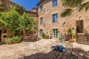 Une cour avec un bâtiment en pierre, des meubles d’extérieur et des plantes en pot.