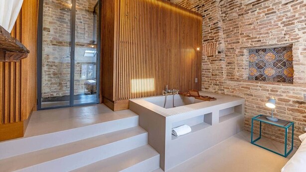 Une salle de bain moderne avec un mur en pierre, une cloison en lattes de bois et une grande baignoire.