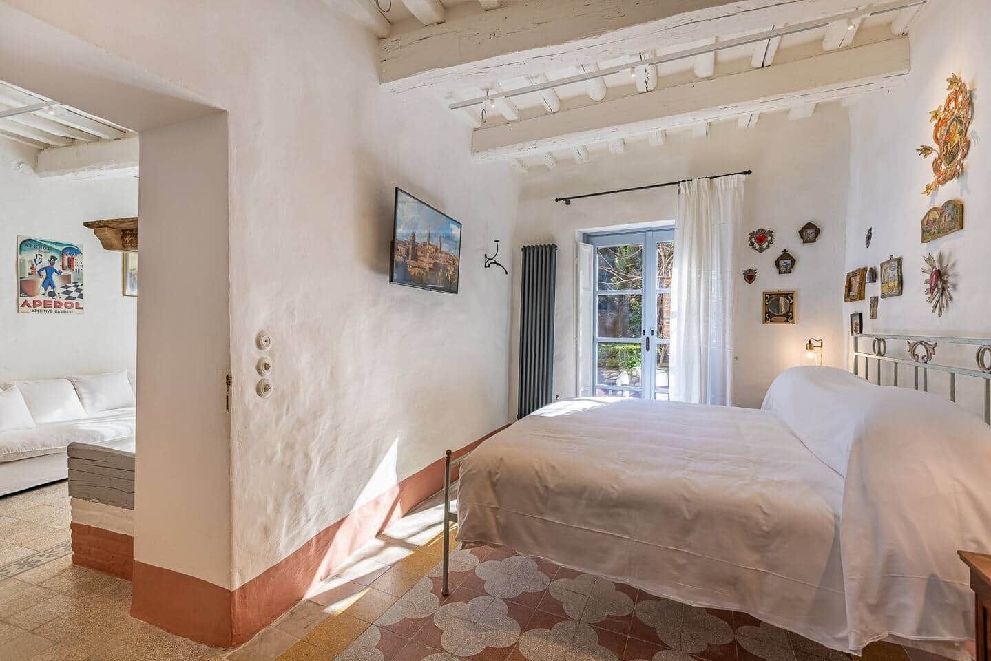 A bedroom with a bed, a window with curtains, a radiator, and a wall with framed pictures.