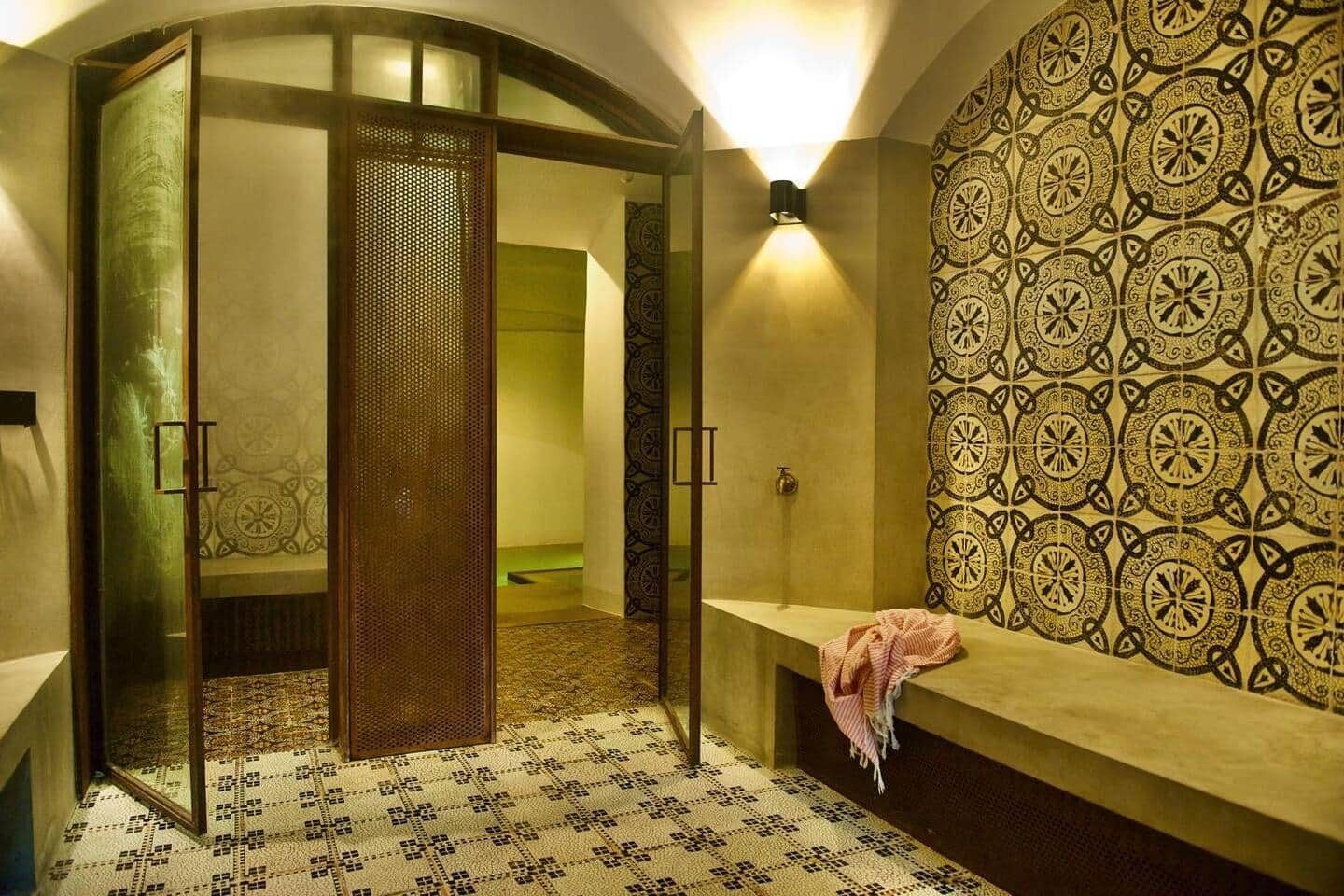 Un bagno con parete decorata, una panca e una porta con un pannello ornamentale.