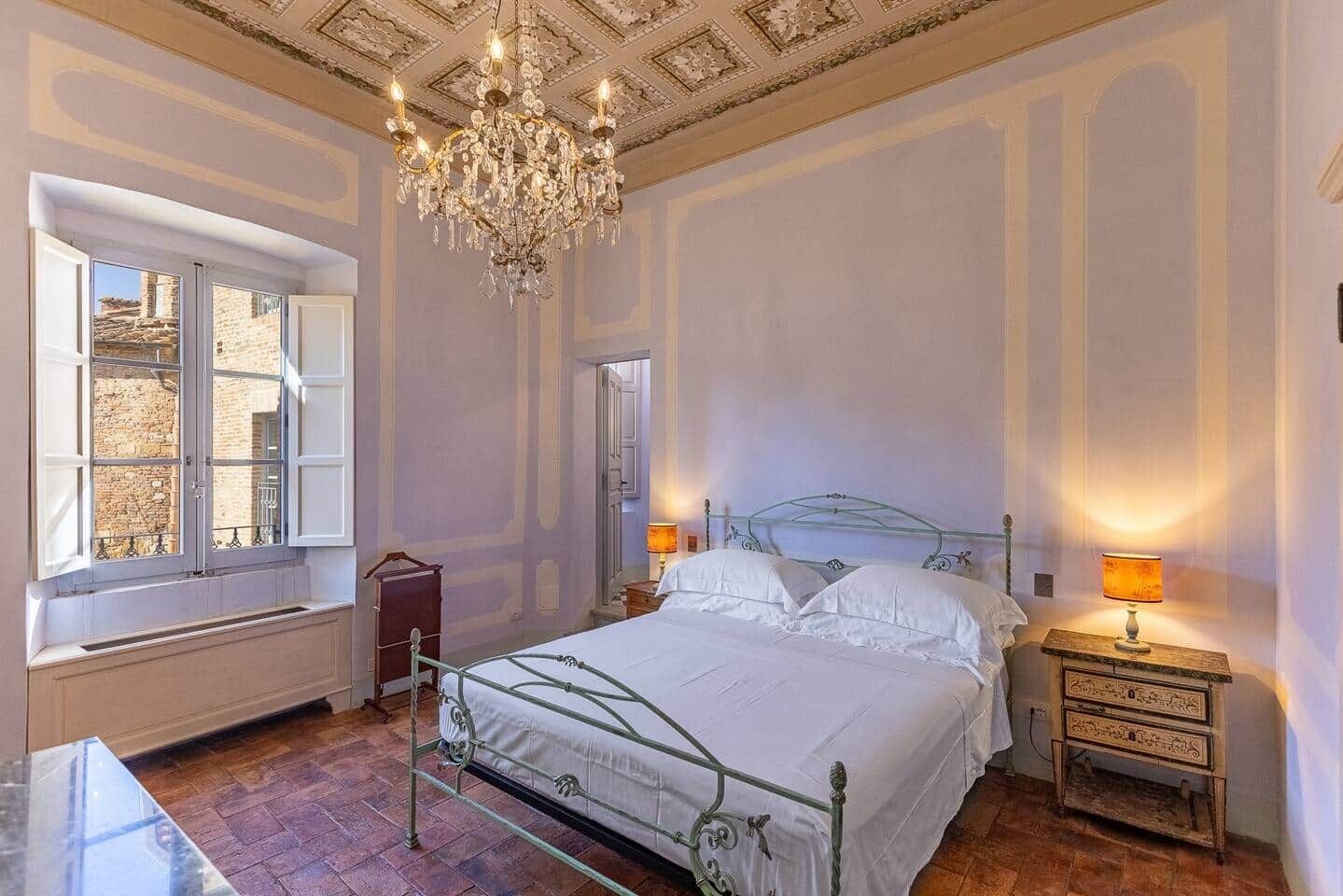 Une chambre à coucher avec un grand lit, un lustre, une fenêtre donnant sur un beau paysage et une table de chevet avec une lampe.