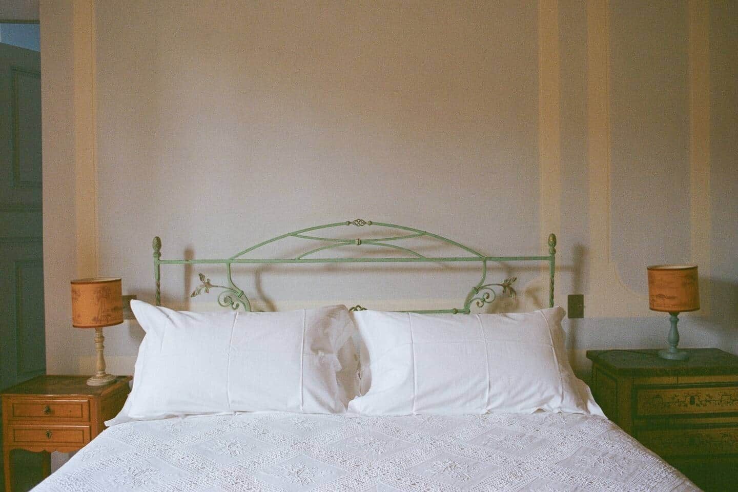 Un lit avec une tête de lit en métal vert, du linge de lit blanc et deux tables de chevet avec des lampes.