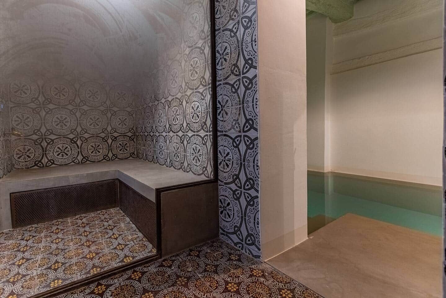 Ein Badezimmer mit gemusterten Fliesen, einer Sitzbank und einer Badewanne.