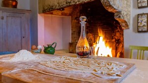 A kitchen with a wooden table, flour, pasta, a green teapot, a glass bottle, and a fireplace in the background. - Donna Lavinia with indoor pool (Città della Pieve)