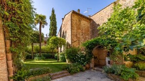 A courtyard with a stone pathway, lush greenery, and a brick building. - Donna Lavinia with indoor pool (Città della Pieve)