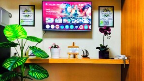 A room with a TV displaying 'The Running Man' on Netflix, a shelf with a plant, a small model ship, and a sign that says 'FOREVERLOVE'. - MOA Staycation Amenity view Escape @ Shell residence (Pasay City)