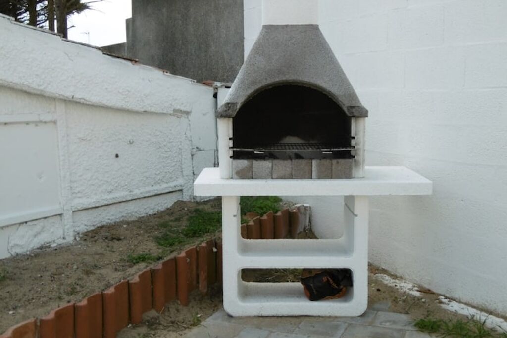 Un horno de pizza de piedra en un pedestal blanco, frente a una pared blanca.