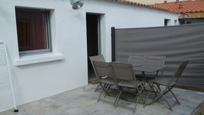 Eine Terrasse mit Tisch und Stühlen, ein Fenster mit Vorhang und eine weiße Wand.