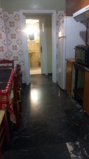 A narrow hallway with a dining table and chairs on the left, a refrigerator and microwave on the right, and a door leading to a bathroom. - Two-room apartment Kalamatas center (Kalamata)