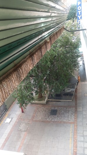 A covered outdoor seating area with a tree, a bench, and a trash bin. - Two-room apartment Kalamatas center (Kalamata)