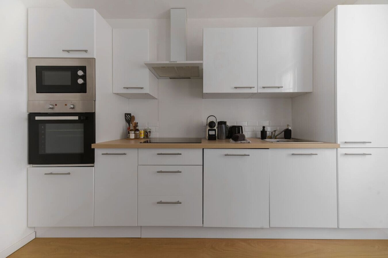 Une cuisine moderne avec des meubles blancs, un four double et une machine à café posée sur le plan de travail.