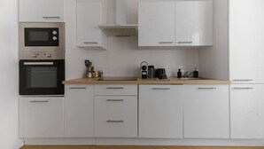 A modern kitchen with white cabinetry, a double oven, and a coffee maker on the countertop. - Appartement calme et lumineux en centre ville (Vichy)