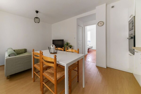 Un espace de vie compact comprenant un coin repas, un canapé, un téléviseur et une kitchenette.