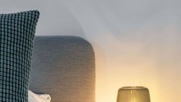 A neatly made bed with a checkered pillow, a bedside lamp, and a wooden nightstand. - Appartement calme et lumineux en centre ville (Vichy)