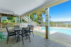 A covered patio with a pool, outdoor seating, and a staircase leading to a deck. - Soundfront | Pool + Game Room + Private Pier (Emerald Isle)
