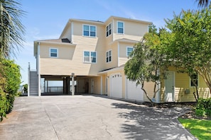 A multi-story residential building with a garage, a covered driveway, and a well-maintained lawn. - Soundfront | Pool + Game Room + Private Pier (Emerald Isle)