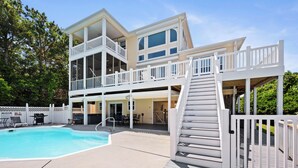 Une maison à deux étages avec une piscine, un espace salon extérieur et une terrasse couverte.
