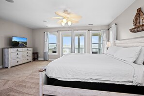 A bedroom with a bed, a dresser, a television, and a balcony with a view. - Soundfront | Pool + Game Room + Private Pier (Emerald Isle)