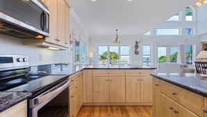 Une cuisine moderne dotée de meubles en bois, d’appareils électroménagers en acier inoxydable et de grandes fenêtres offrant une vue sur l’extérieur.
